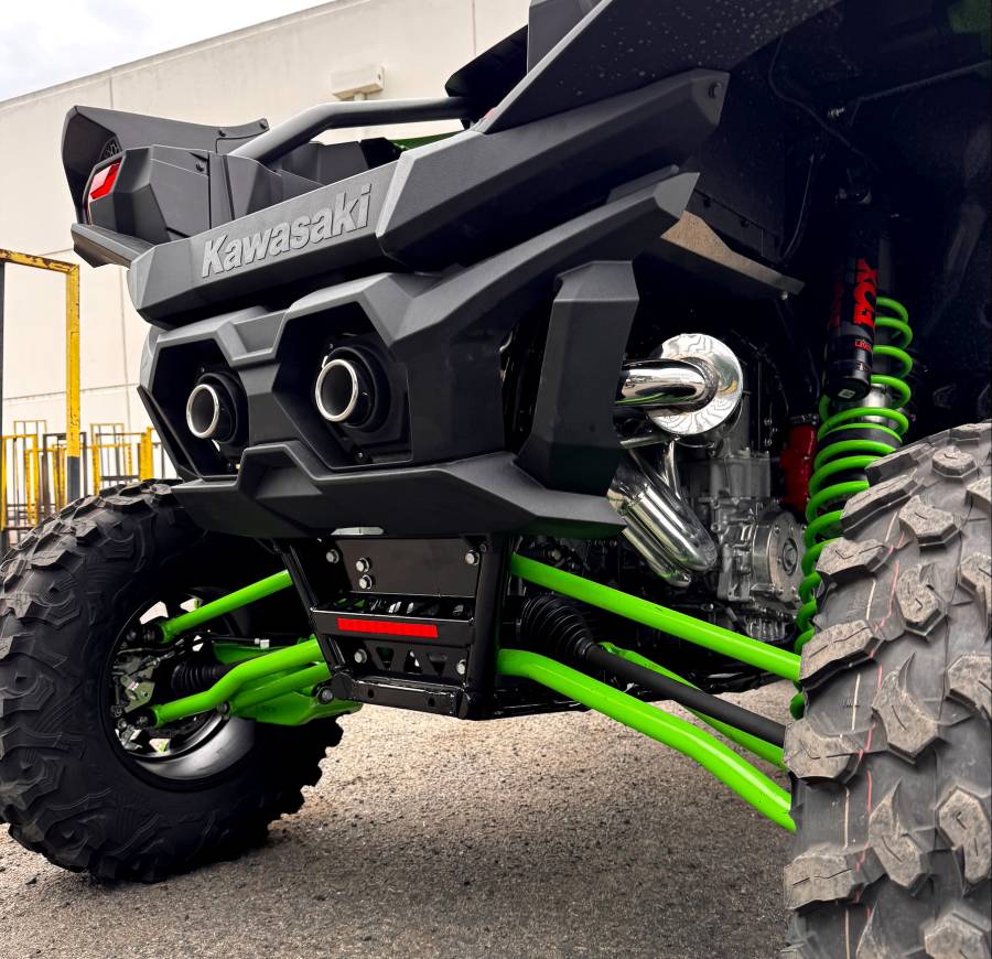 Close-up of a Kawasaki ATV with green suspension and tires on a concrete surface.