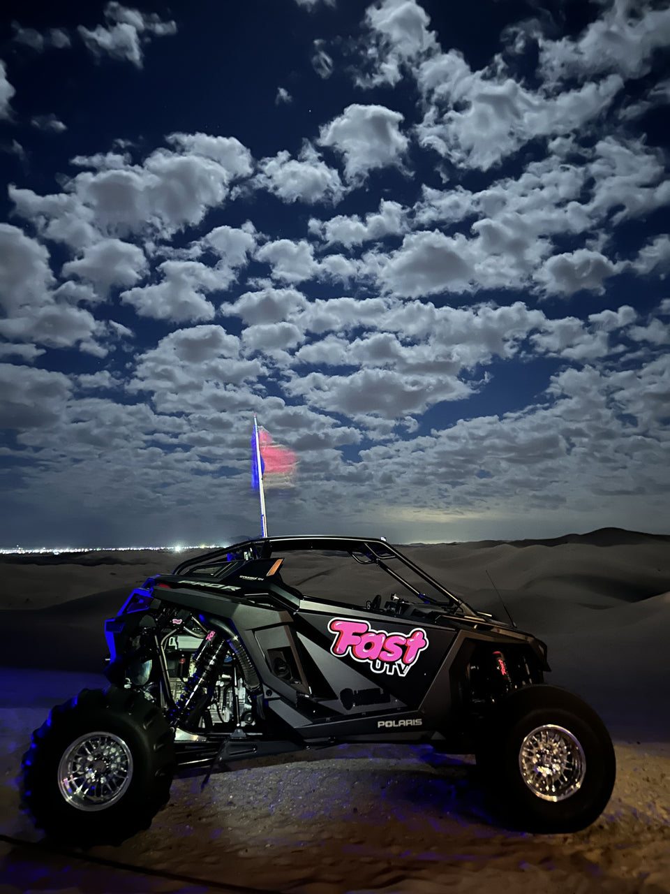 UTV de FastUTV con iluminación azul y una bandera estacionado en las dunas de noche