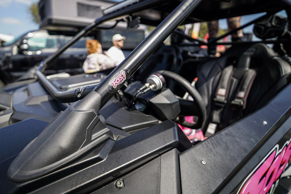 Primer plano de una placa de FastUTV en la jaula antivuelco, el volante y el arnés del asiento de un UTV