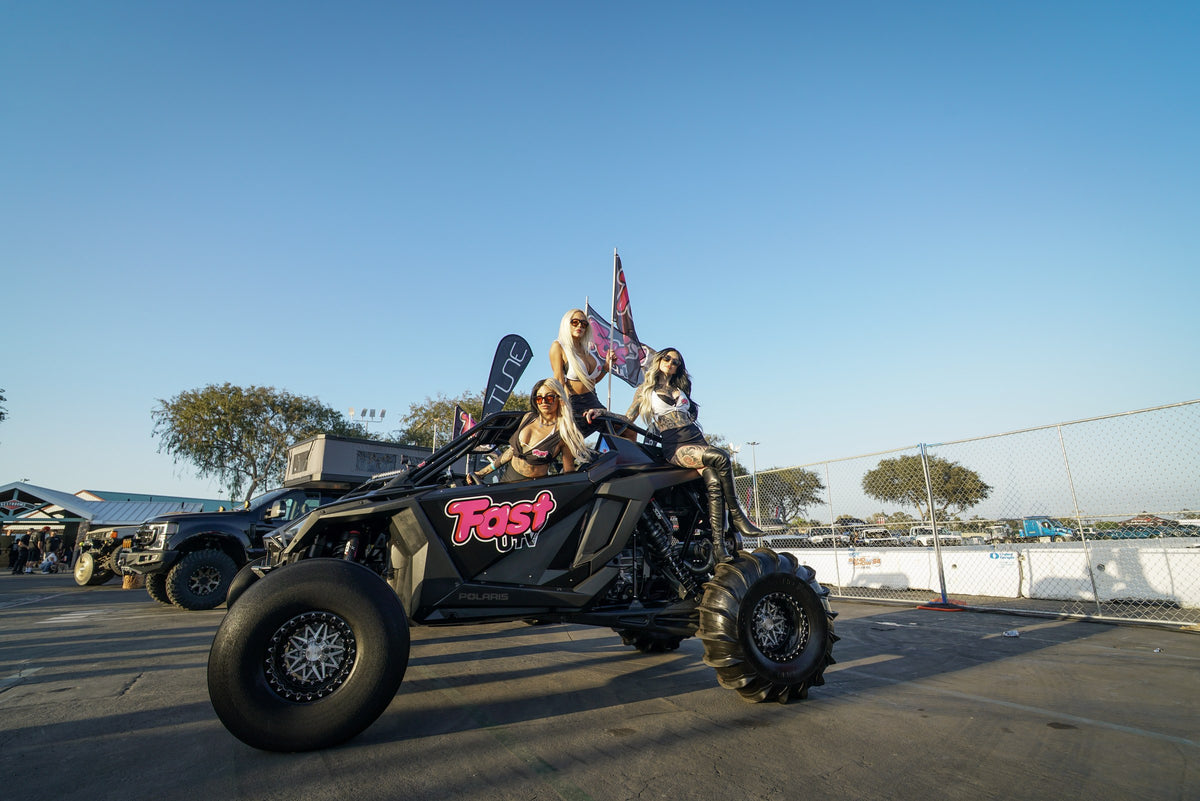 UTV negro de FastUTV con neumáticos de paletas, tres modelos y banderas en la exposición