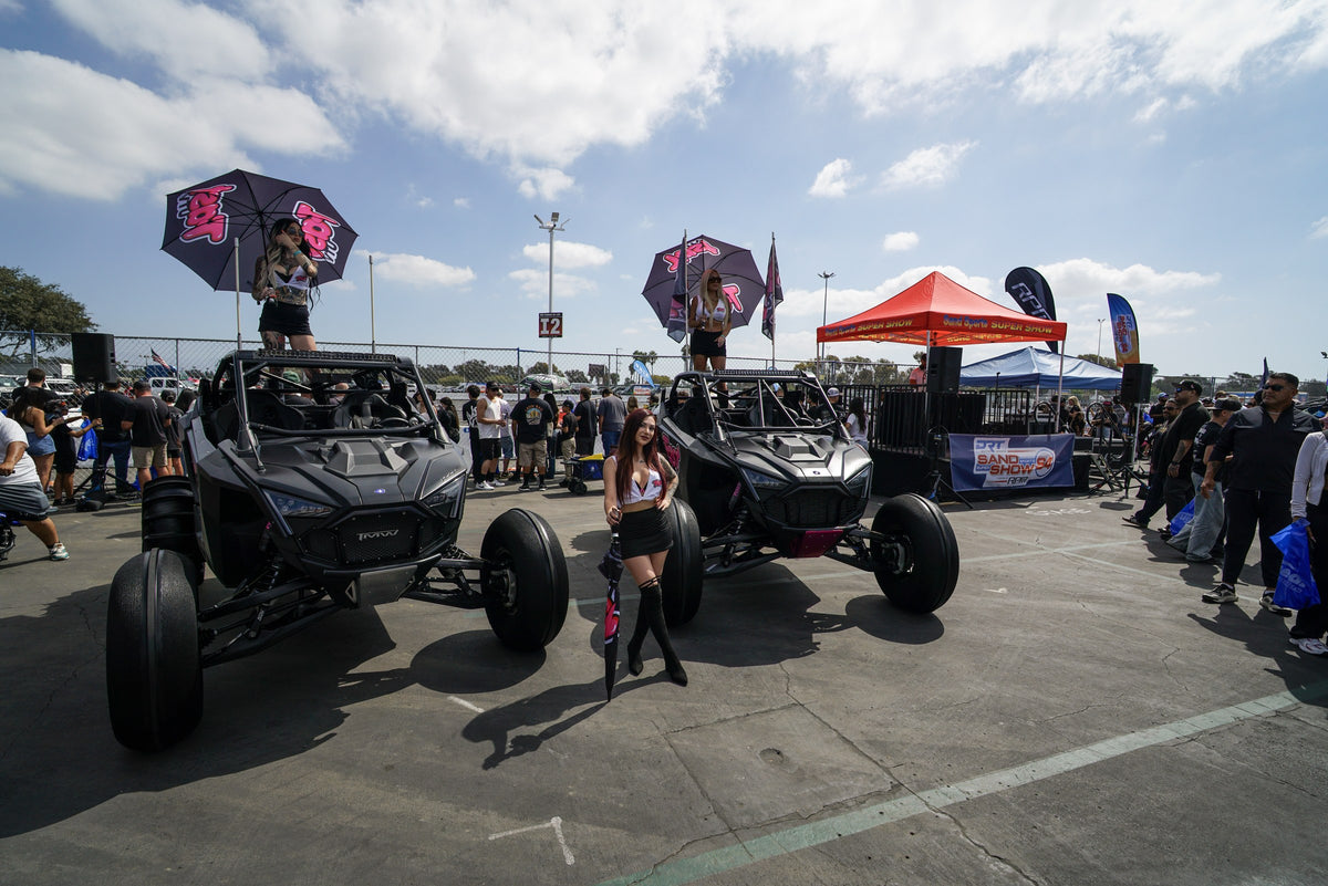 Two black UTVs with three models and FastUTV umbrellas in a busy show display
