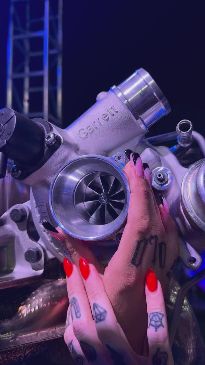 Models inspecting a Garrett turbocharger display under blue lighting