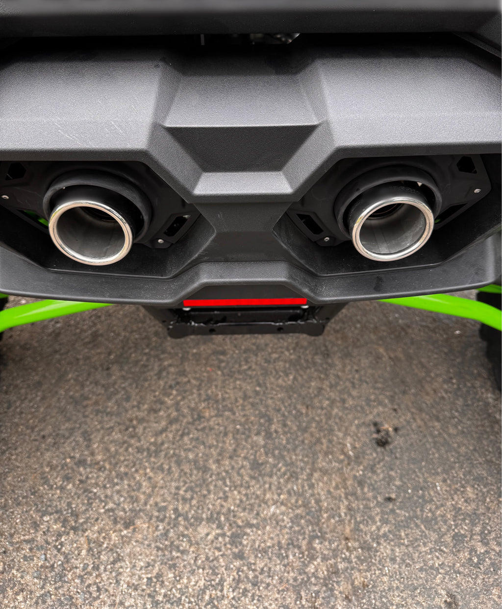 Wide rear-angle view of polished exhaust tips installed on a Kawasaki TERYX4 H2, shown beneath the factory bumper with a clean off-road finish.
