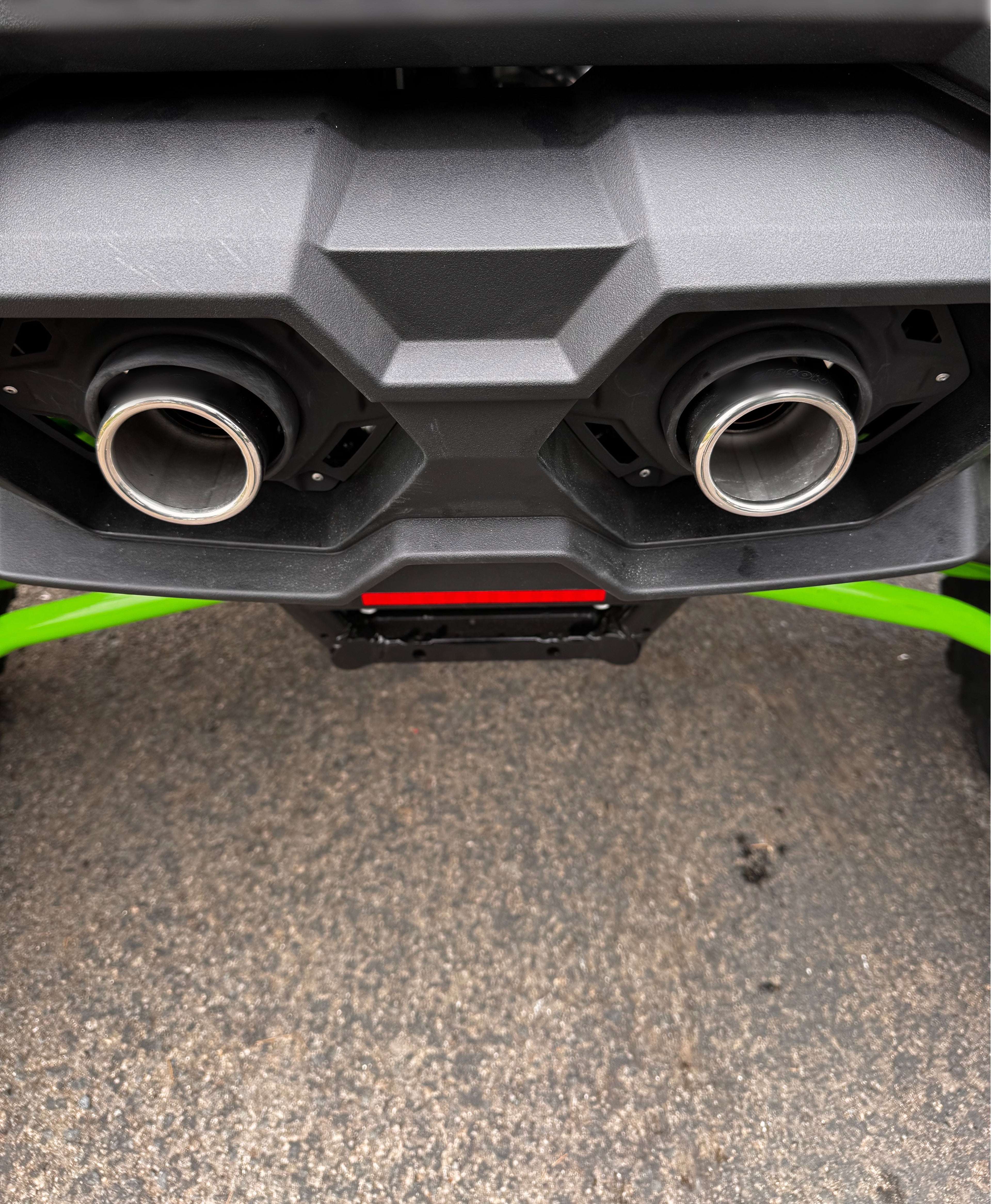 Wide rear-angle view of polished exhaust tips installed on a Kawasaki TERYX4 H2, shown beneath the factory bumper with a clean off-road finish.