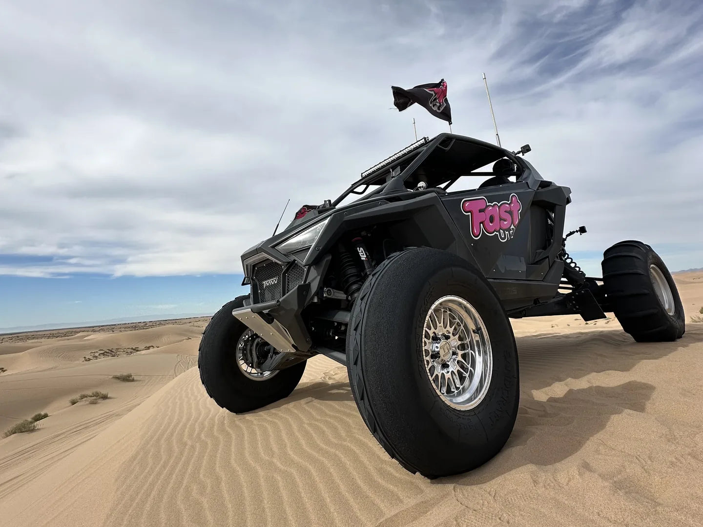 Full FastUTV UTV and flag on a sand dune beneath a bright sky